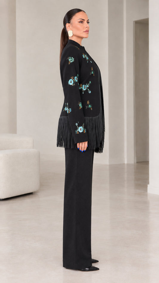 Side angle view of black embroidered blazer with fringe trim and tailored pants
