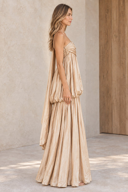 Side profile view of champagne one-shoulder pleated evening gown showing fluid volume and drape
